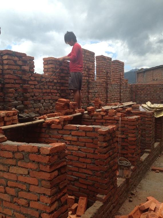 A mason standing on the half-built brick walls of the new girls’ bathroom block.