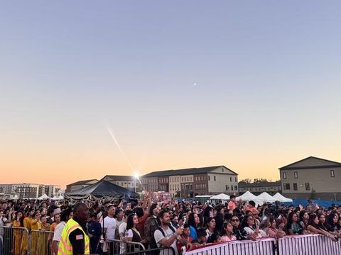 Thousands of festival-goers filling the fairground at sunset.