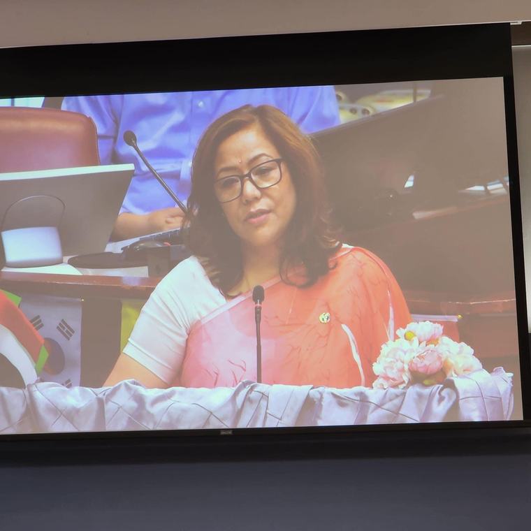 Prabha Bhattarai Deuja speaking, shown on a large presentation screen.