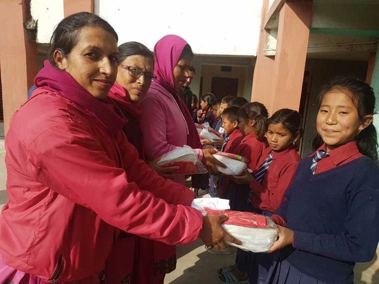 Prabha Bhattarai handing a shoebox to a smiling schoolgirl in uniform.