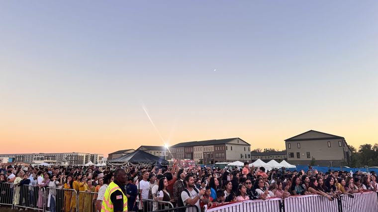 Thousands of festival-goers filling the fairground at sunset.