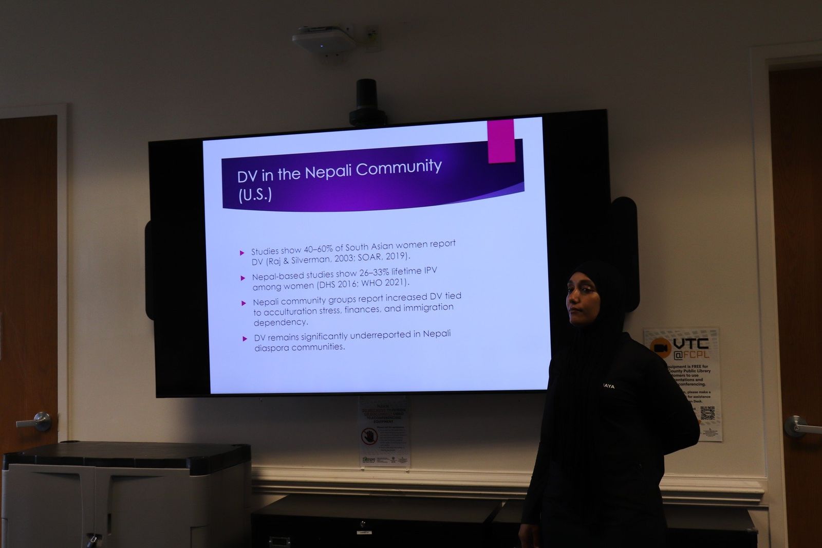 A presenter addressing attendees in front of a slide about resources for the Nepali community.